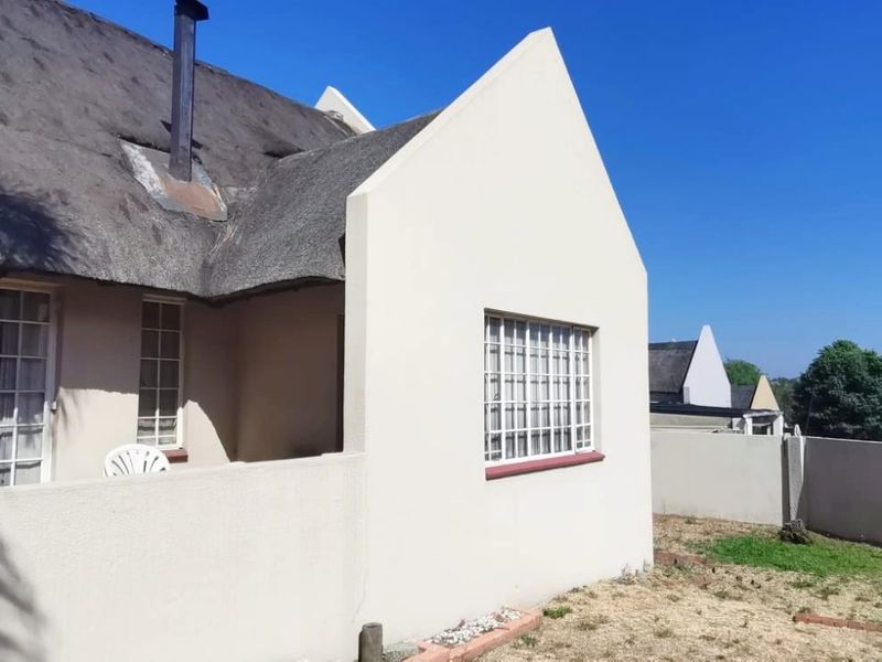 Rear view of a house featuring a traditional thatch roof, chimney, and a private garden area with boundary walling.