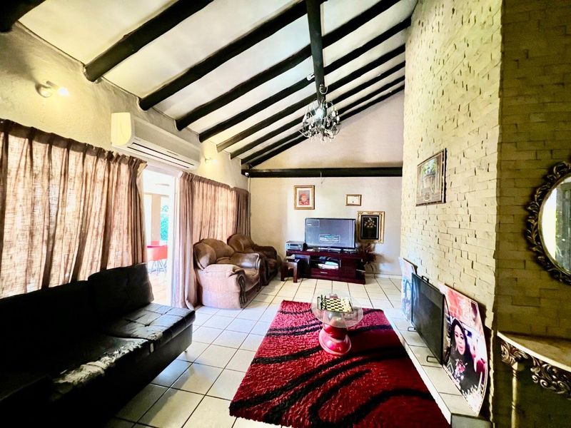 Spacious living room featuring a vaulted ceiling with exposed timber beams, a prominent stone-clad fireplace, and direct access to an outdoor patio area.