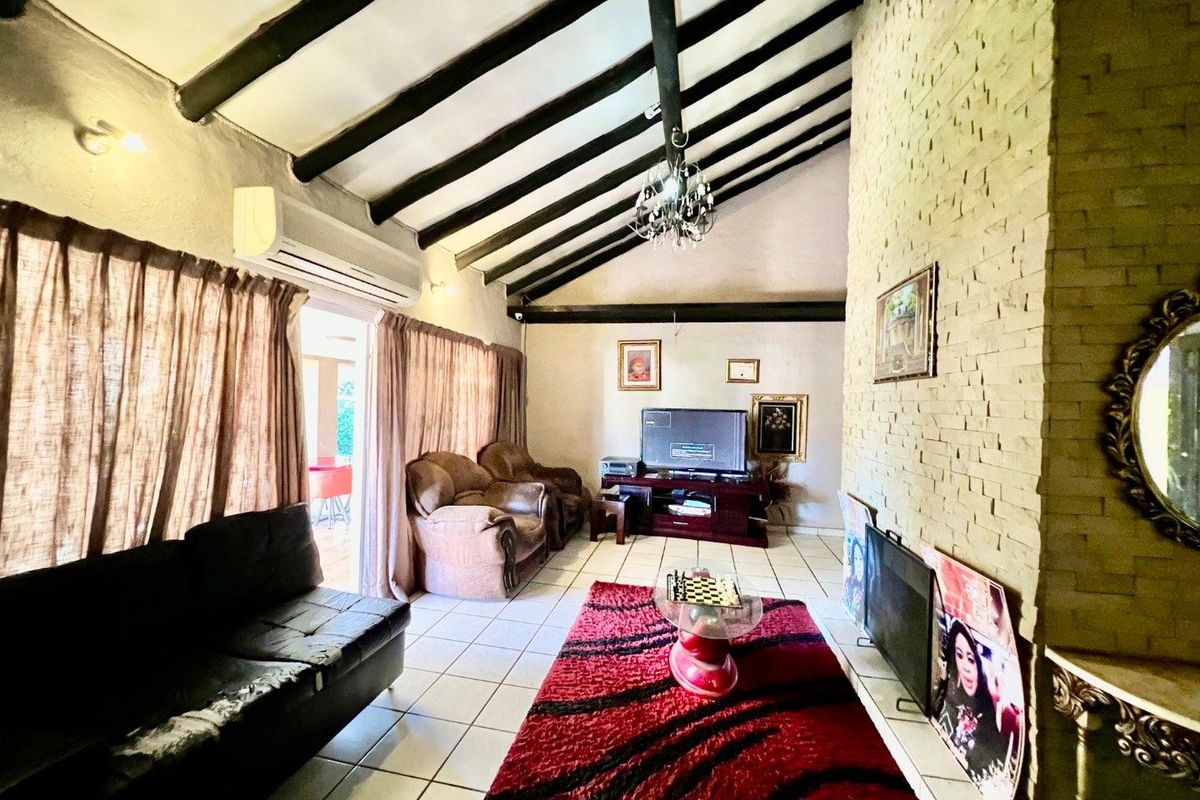 Spacious living room featuring a vaulted ceiling with exposed timber beams, a prominent stone-clad fireplace, and direct access to an outdoor patio area.