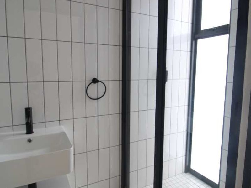 Modern bathroom featuring a wall-mounted vanity, black tapware, and a walk-in shower with a rain shower head and contemporary white tiling.