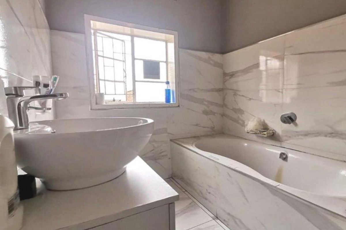 A bathroom featuring marble-look wall and floor tiles, a modern vessel sink, and a built-in bathtub with a window for natural light.