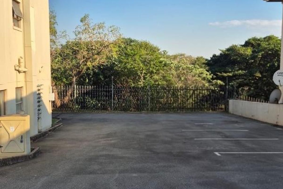 An outdoor parking area located at the rear of the apartment building, featuring asphalt paving and perimeter security fencing.