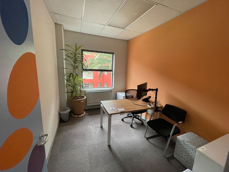 A functional office space featuring carpeted flooring, a suspended ceiling, and a window with an integrated HVAC unit.