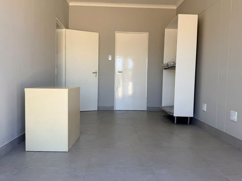 A clean, empty office space featuring neutral grey walls, large format floor tiles, and white internal doors, ready for professional use.