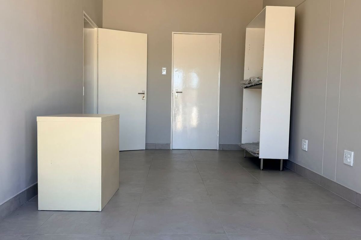 A clean, empty office space featuring neutral grey walls, large format floor tiles, and white internal doors, ready for professional use.