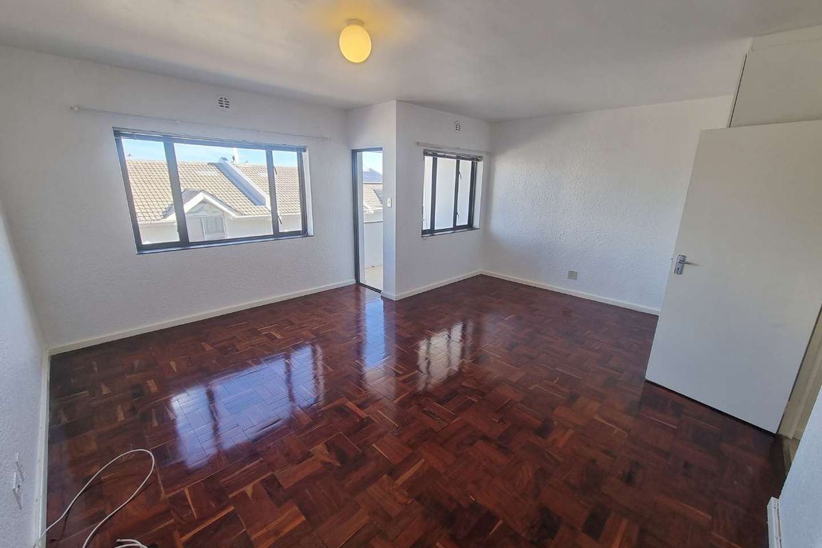A bright, empty bedroom featuring polished parquet flooring, white walls, and a built-in cupboard, offering a clean canvas for personalization.