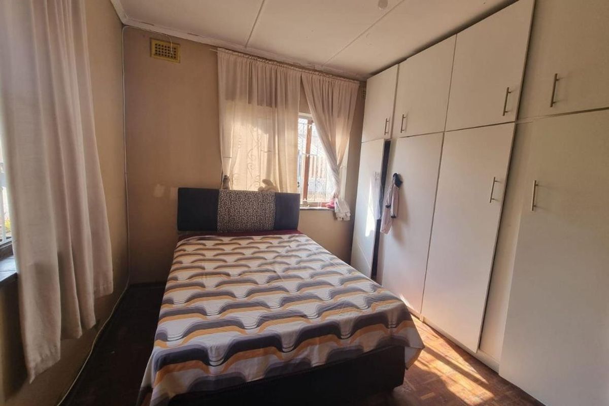 A bedroom featuring built-in cupboards and parquet flooring, offering a functional space with potential for cosmetic updates.