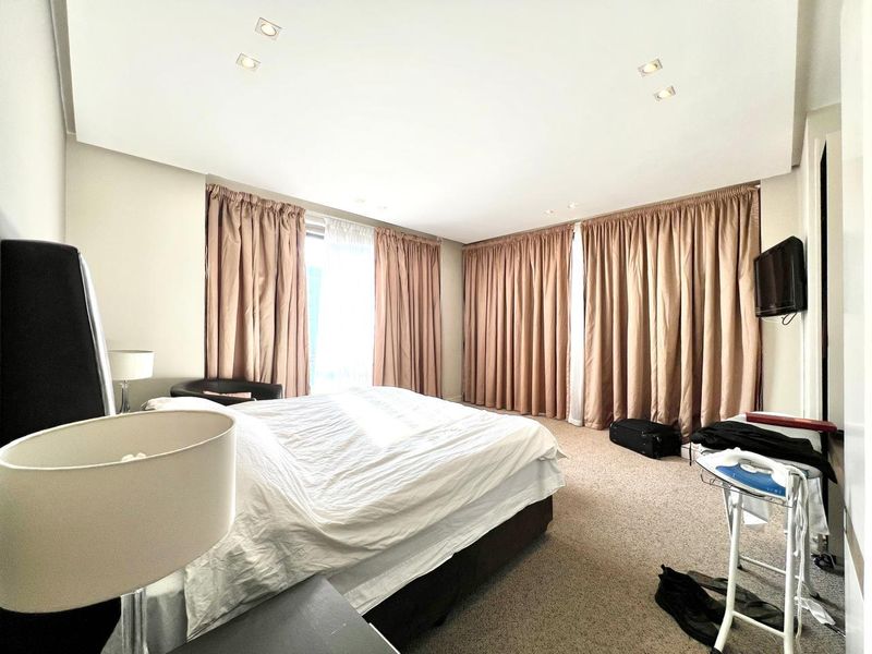 A spacious bedroom featuring neutral wall tones, wall-to-wall carpeting, recessed downlighting, and full-height curtains providing access to natural light.