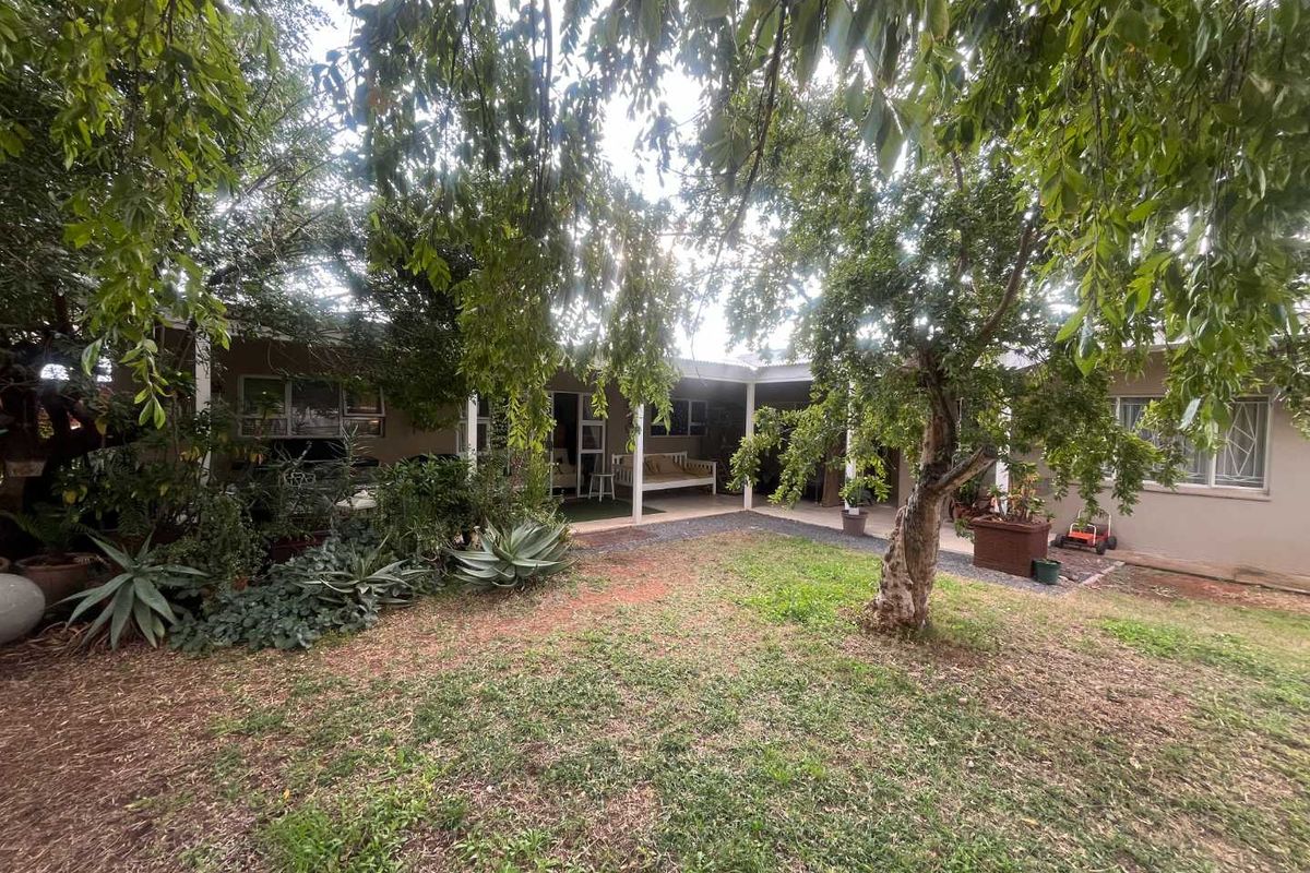 A view of the rear garden and patio area, featuring mature trees, established landscaping, and a covered outdoor living space.