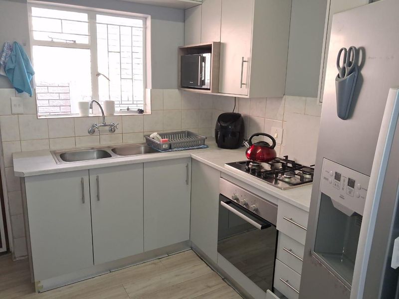 A functional kitchen featuring light grey cabinetry, a gas hob, built-in oven, microwave, and a double basin sink with tiled backsplash.