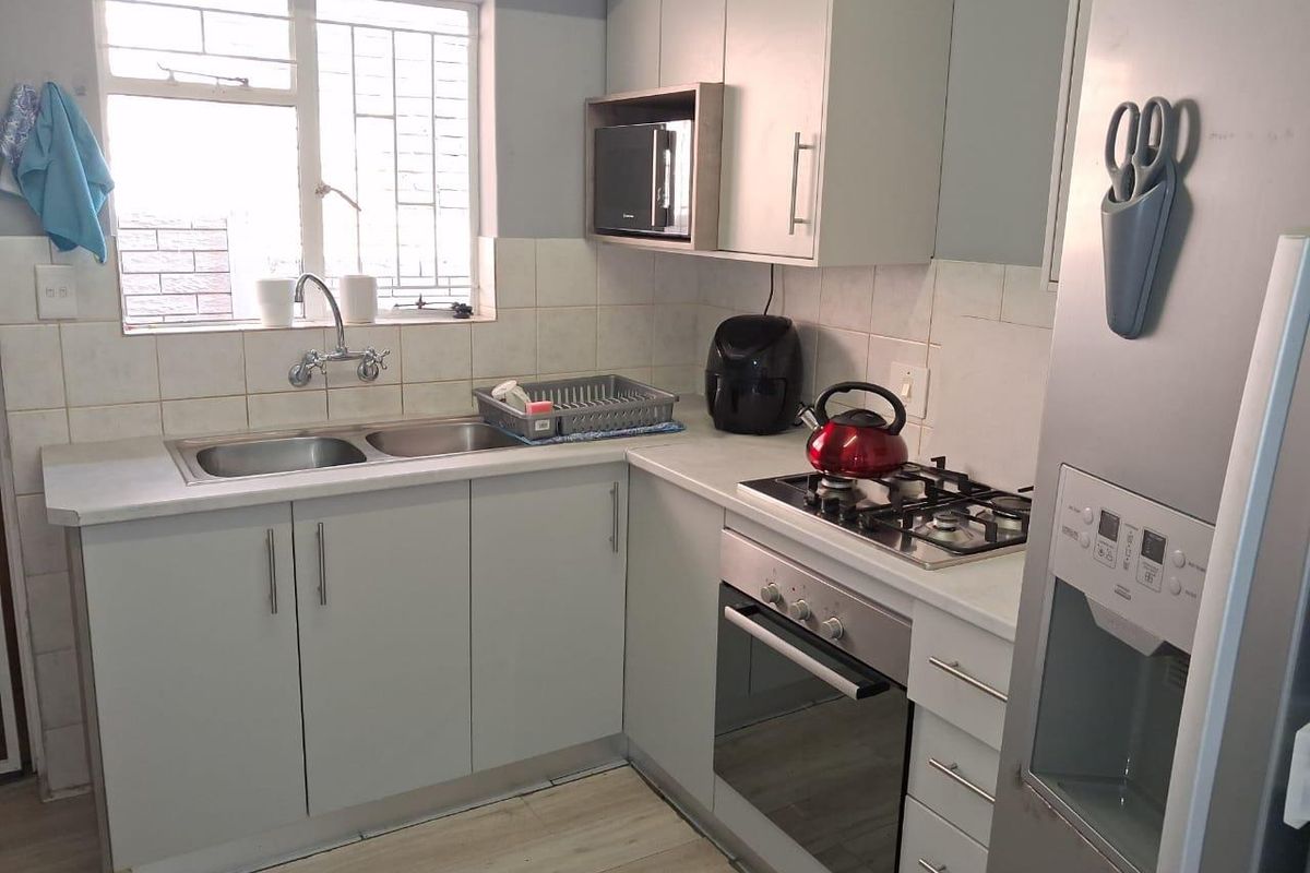 A functional kitchen featuring light grey cabinetry, a gas hob, built-in oven, microwave, and a double basin sink with tiled backsplash.