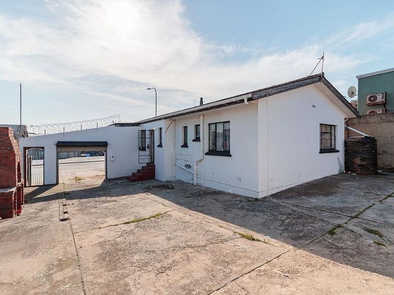 Rear exterior view of the office property featuring a concrete paved yard, brick braai, water tank, and security fencing.