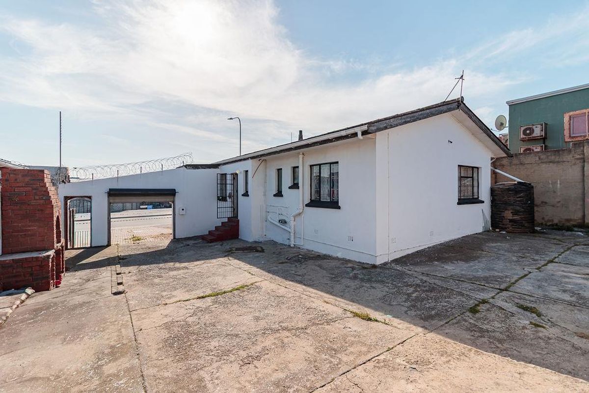 Rear exterior view of the office property featuring a concrete paved yard, brick braai, water tank, and security fencing.