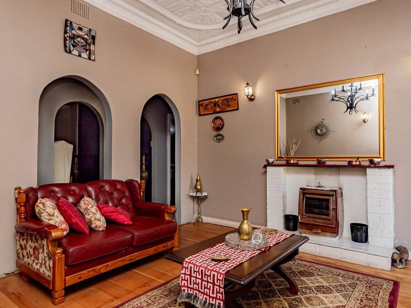 A classic living room featuring a fireplace with a brick hearth, decorative ceiling molding, hardwood flooring, and distinctive arched doorways leading to adjacent spaces.