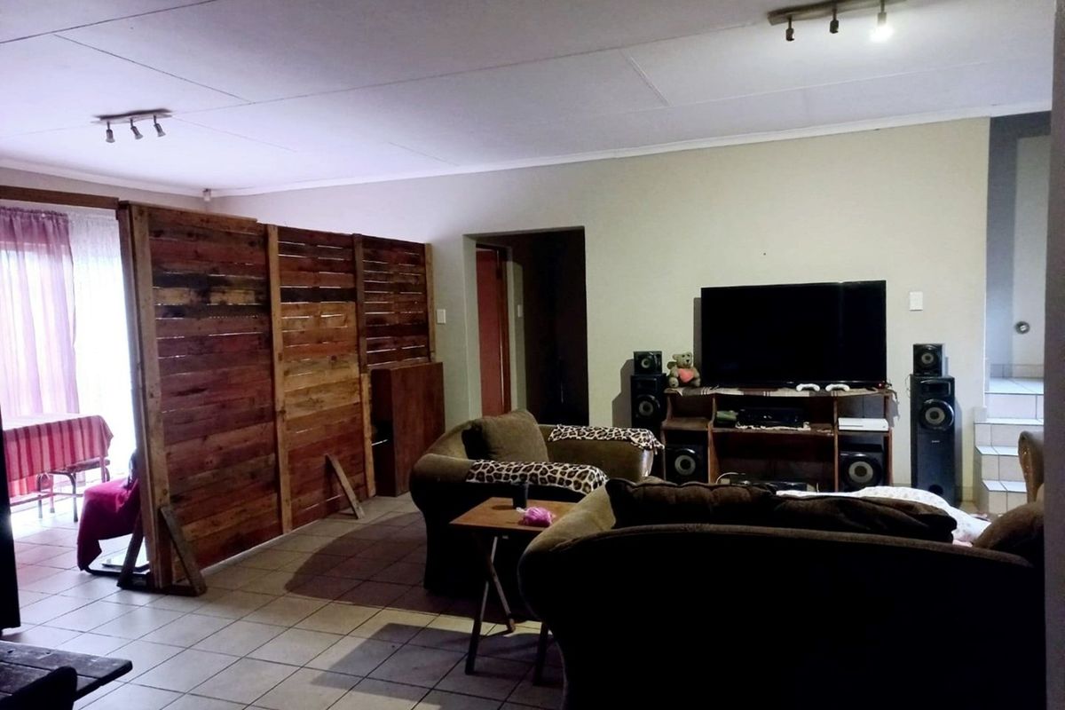 A living room area featuring tiled flooring and track lighting, currently partitioned with a wooden screen.
