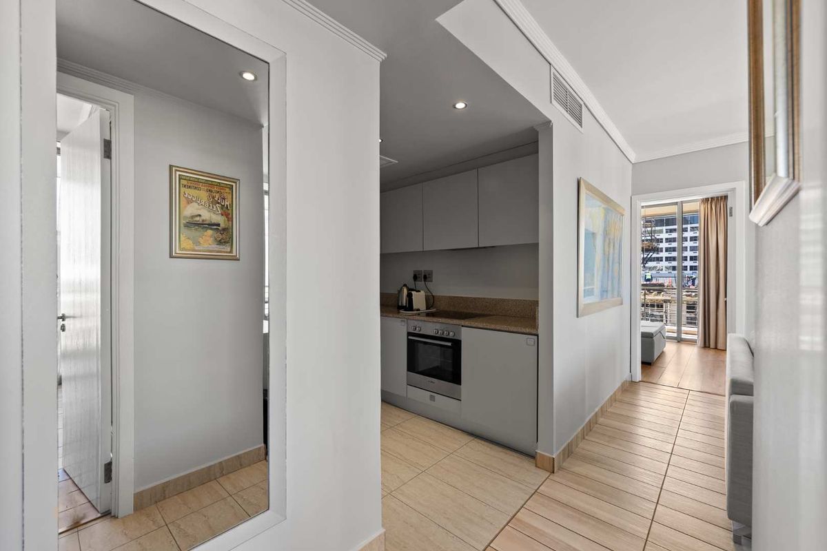 A compact, modern kitchen featuring built-in cabinetry, integrated oven and hob, and neutral tiled flooring, seamlessly connected to the living area.