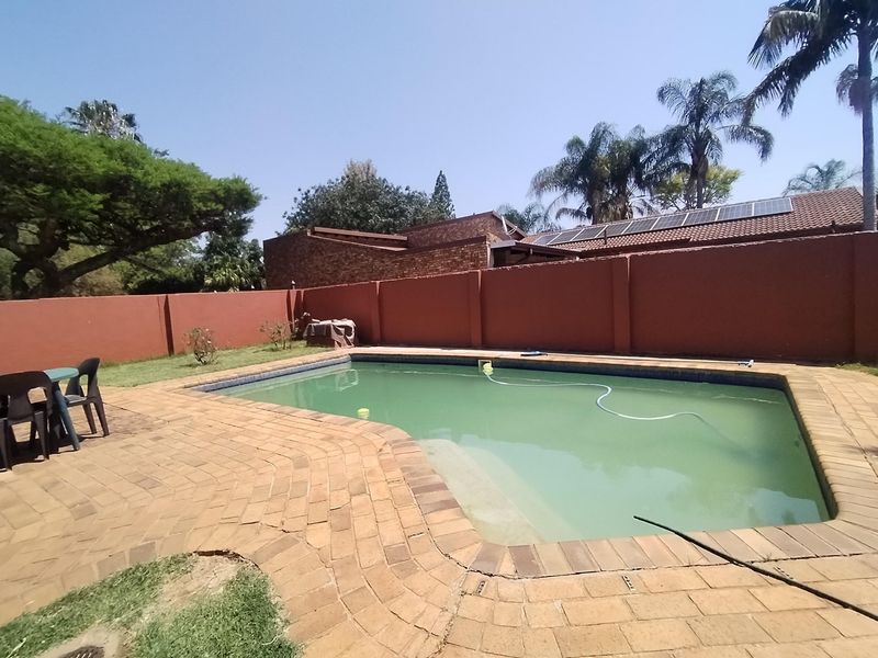 Outdoor pool area featuring a swimming pool with brick paved surround and high boundary walls, set within a private garden space.