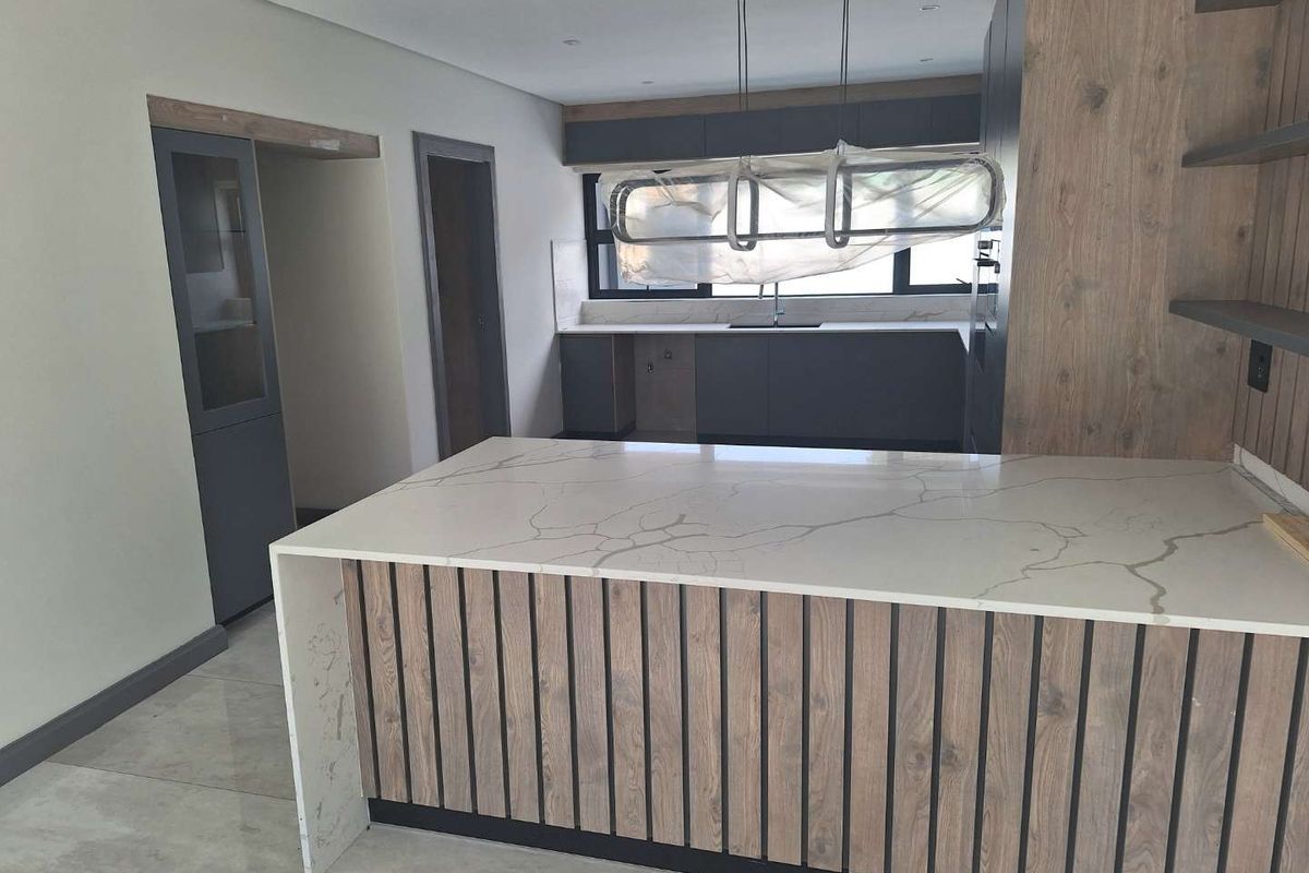 Modern kitchen featuring a large island with quartz countertop, wood-panel detailing, and sleek dark cabinetry. The space is currently undergoing final finishing touches.