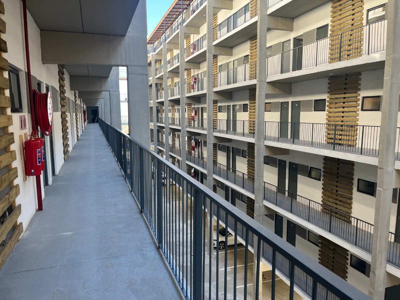 An exterior apartment complex hallway featuring concrete walkways, metal balustrades, and integrated fire safety equipment with modern timber facade detailing.