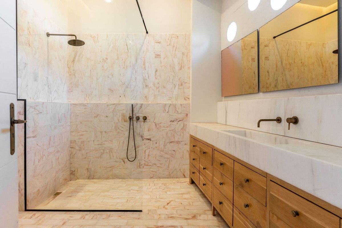 Modern bathroom featuring a walk-in shower with marble tiling, a custom wooden vanity with integrated marble sink, and wall-mounted brass fixtures.