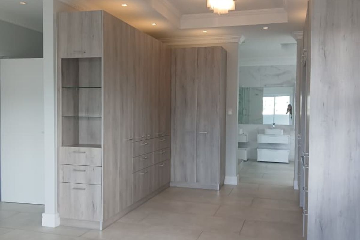 Spacious dressing room featuring extensive built-in cabinetry with light wood finish, recessed ceiling lighting, and large format floor tiles leading to an en-suite bathroom.