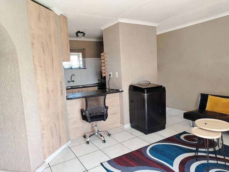 Open-plan living area featuring a compact kitchen with built-in cabinetry, a breakfast bar, and tiled flooring throughout.