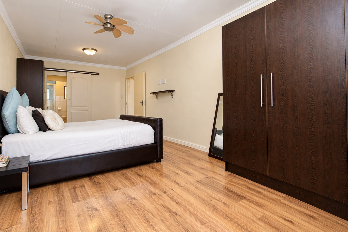 A well-maintained bedroom featuring laminate flooring, built-in dark wood cupboards, a ceiling fan, and direct access to an en-suite bathroom.