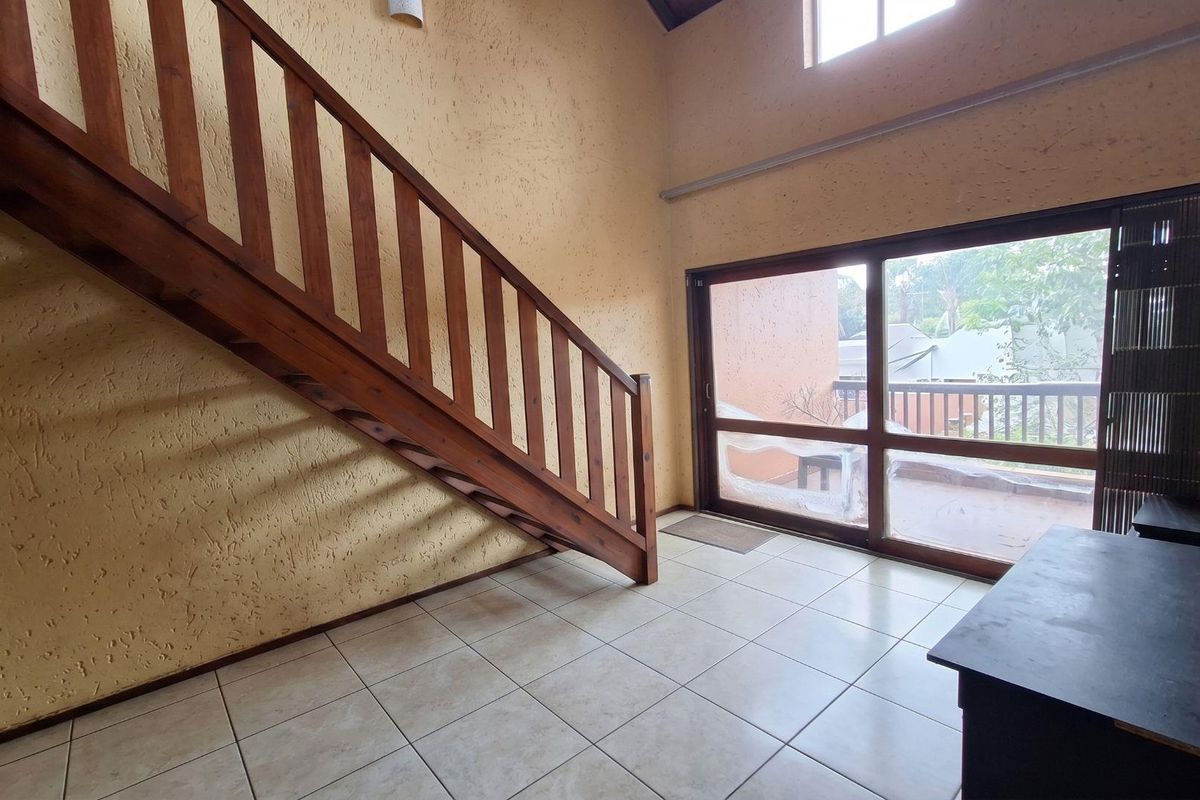 Spacious living area featuring a wooden staircase, high ceilings, tiled flooring, and large sliding glass doors leading to an outdoor balcony.