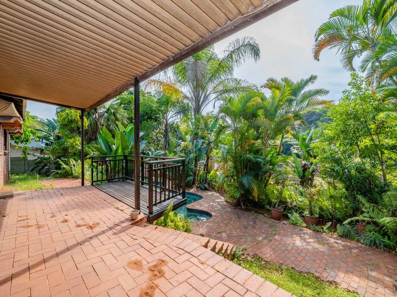 A covered brick patio area featuring a small timber deck and access to a garden pool, offering a tranquil outdoor living space.