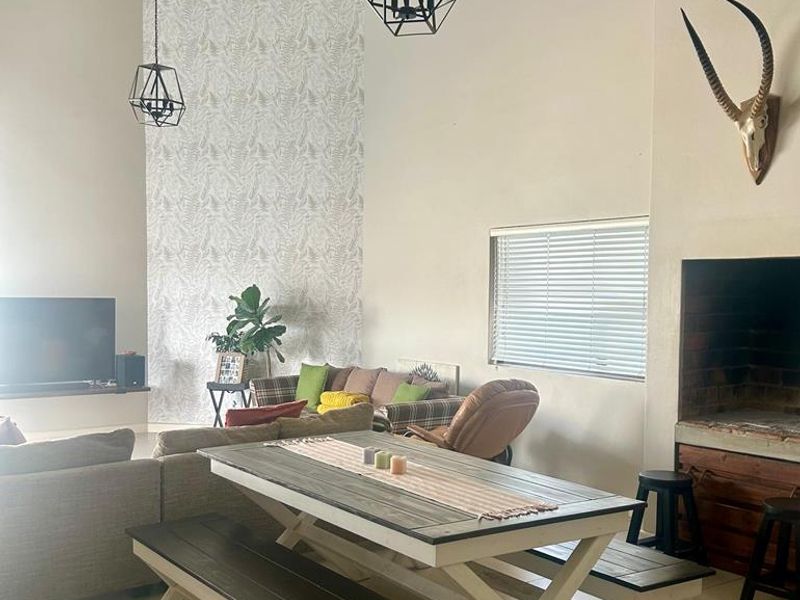 Spacious open-plan living and dining area featuring high vaulted ceilings with exposed rafters, tiled flooring, and a built-in fireplace.