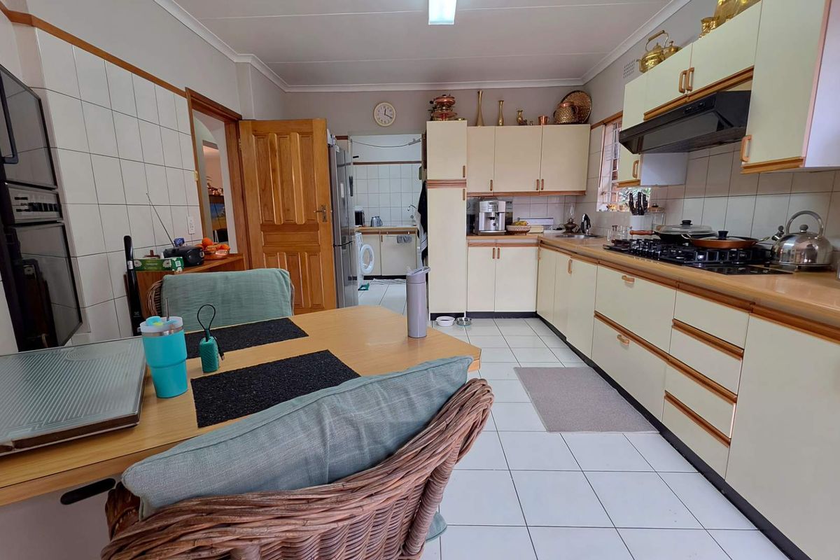 A functional kitchen featuring light-toned cabinetry, tiled flooring, a built-in oven, and a gas hob, with an adjacent scullery area visible.