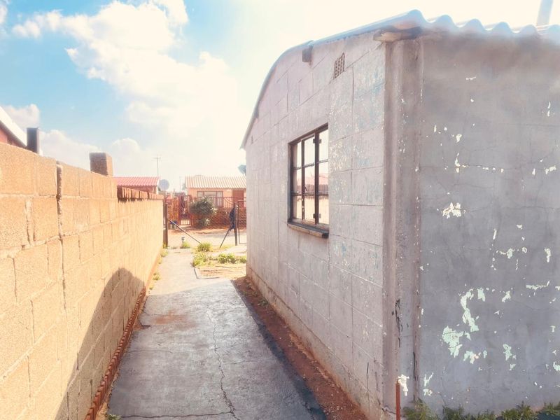 A side view of the property showing a concrete block wall, a steel window frame, and a concrete pathway leading to the rear area.