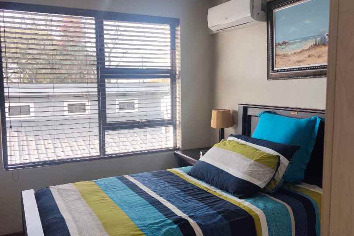 A well-maintained bedroom featuring tiled flooring, aluminium window frames with venetian blinds, and a wall-mounted split-system air conditioner.