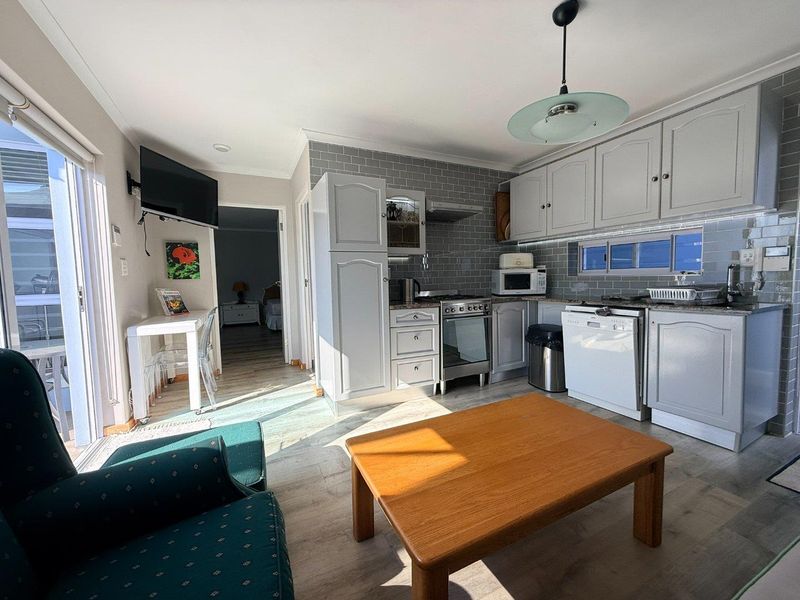 Open-plan kitchen and living area featuring grey shaker-style cabinetry, subway tile backsplash, granite countertops, and direct access to an outdoor patio area.
