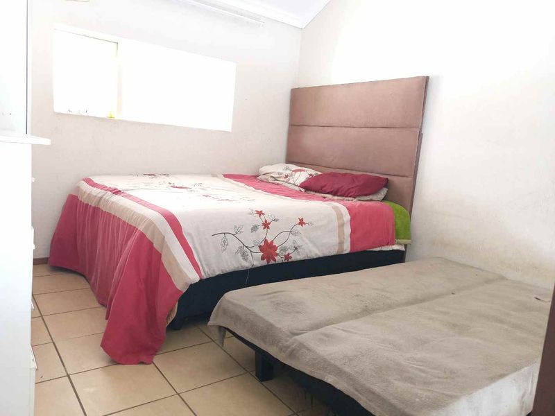 A bedroom featuring tiled flooring and a window, currently showing signs of wear on the wall surfaces.