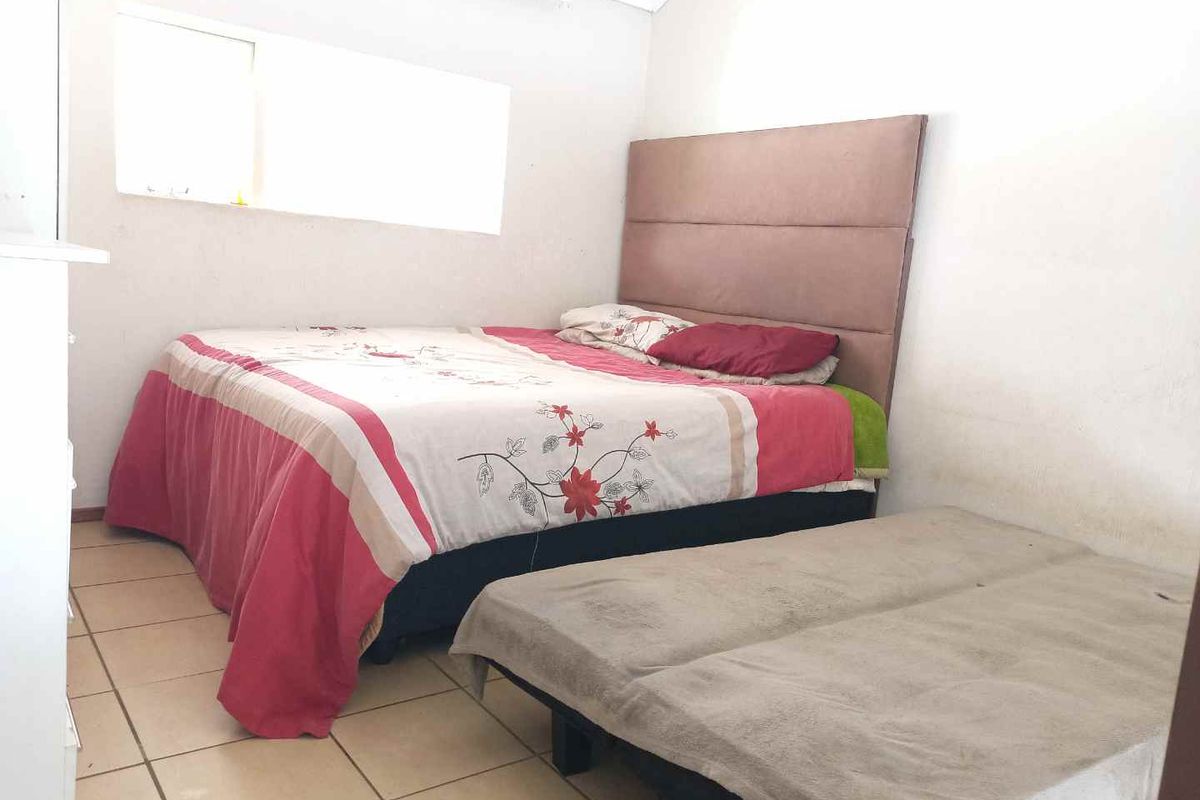 A bedroom featuring tiled flooring and a window, currently showing signs of wear on the wall surfaces.