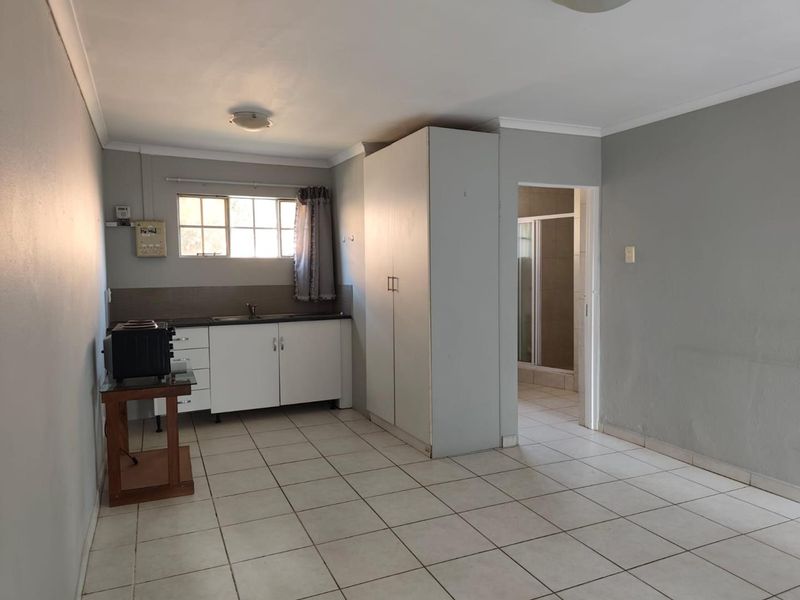 Open plan living area featuring tiled flooring, built-in kitchen cabinetry with sink, and a built-in cupboard, with direct access to an adjoining bathroom.