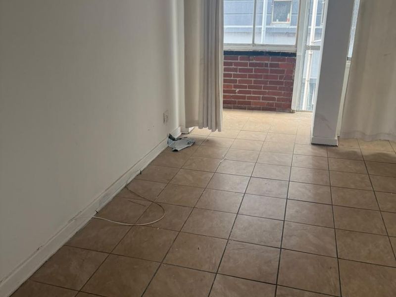 An empty living area featuring ceramic floor tiles and a sliding glass door leading to a small balcony with a brick wall.