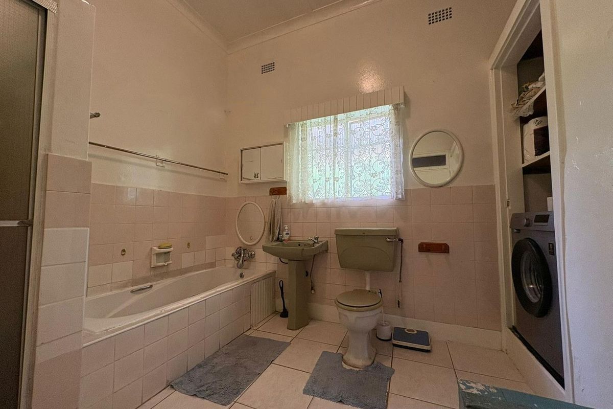 A dated bathroom featuring a built-in bathtub, pedestal sink, toilet, and integrated laundry space with tiled walls and flooring.