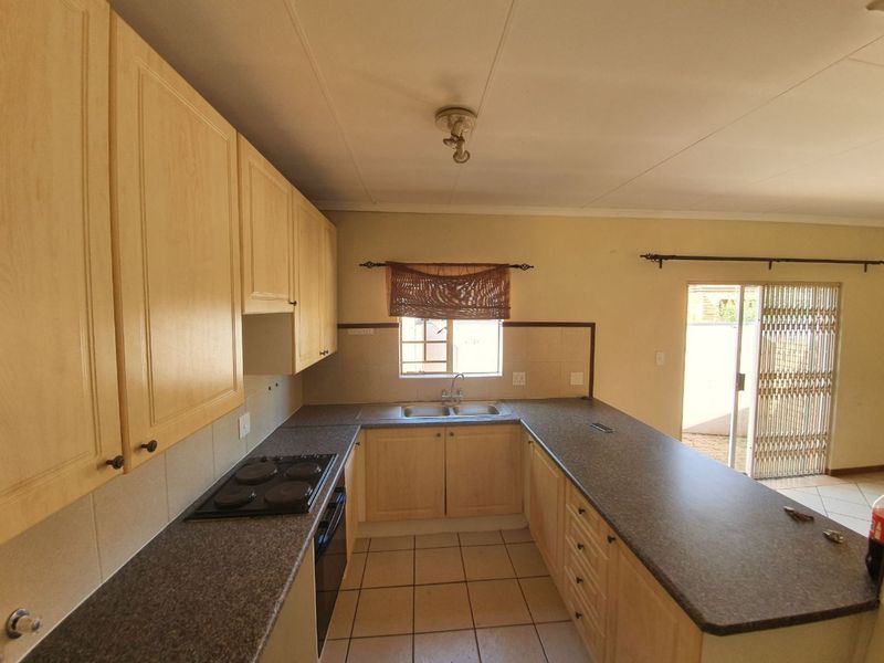 Functional kitchen featuring light wood cabinetry, dark laminate countertops, built-in oven and hob, and direct access to an outdoor patio area.