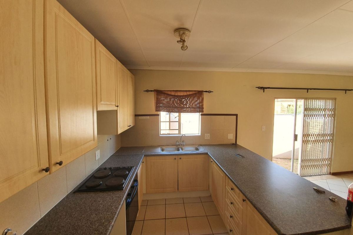 Functional kitchen featuring light wood cabinetry, dark laminate countertops, built-in oven and hob, and direct access to an outdoor patio area.