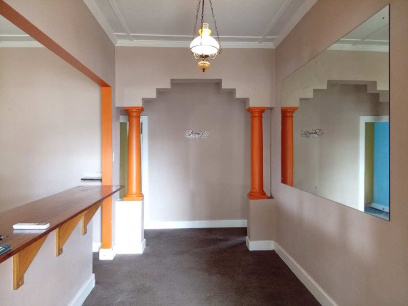 An empty living area featuring a built-in bar counter, decorative columns, a stepped archway, and a large wall-mounted mirror.