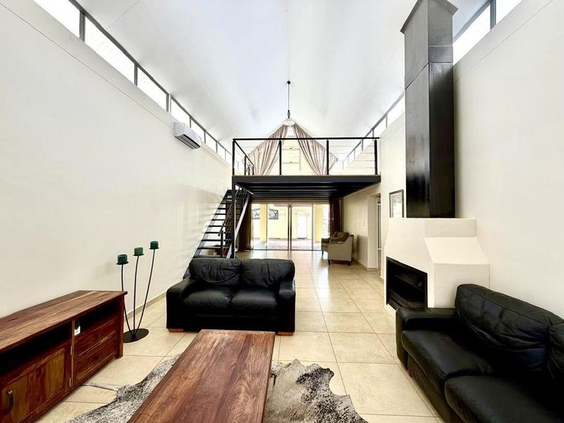 Spacious living area featuring a double-volume vaulted ceiling, mezzanine level, modern fireplace, and large clerestory windows providing abundant natural light.