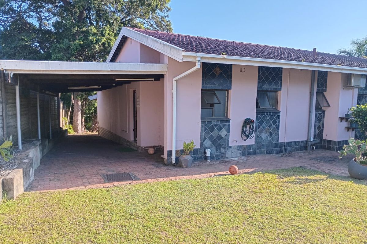 A side view of a residential house featuring a covered carport, brick paved driveway, and tiled exterior wall accents.