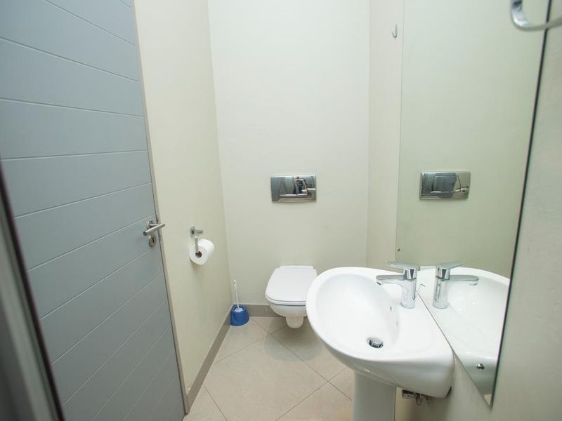 A clean and functional guest bathroom featuring a wall-mounted toilet, pedestal basin, and large wall mirror.