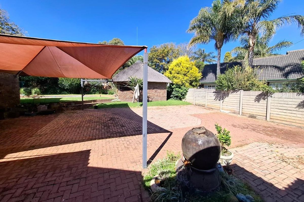 A spacious rear garden featuring a paved patio area with a shade sail, a thatched lapa, and perimeter precast concrete walling.