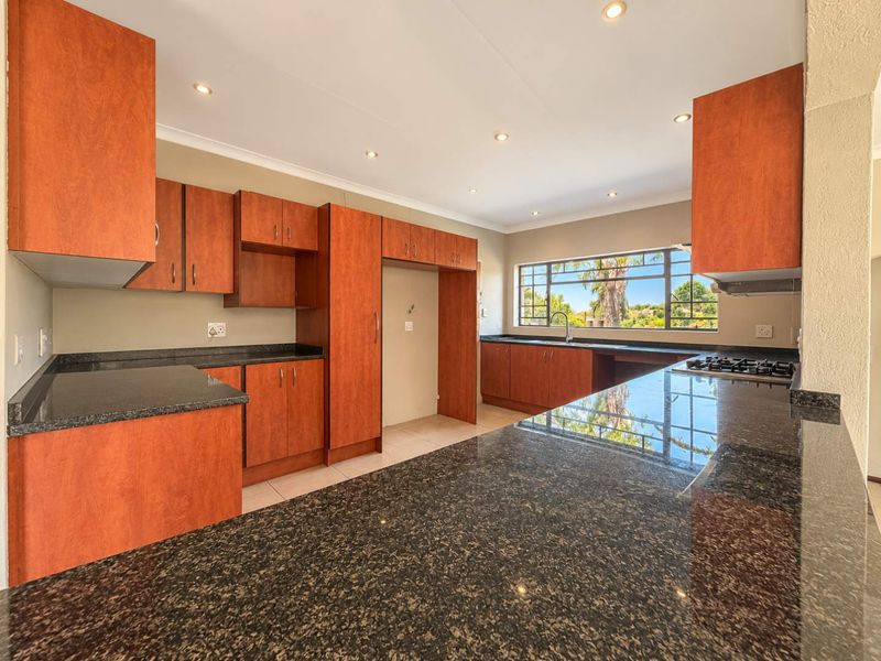 Spacious kitchen featuring dark granite countertops, ample wooden cabinetry, a built-in gas hob, and large windows providing natural light and garden views.