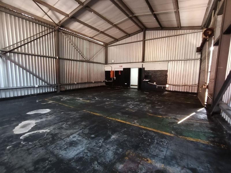 Spacious industrial warehouse unit featuring high ceilings, exposed steel trusses, corrugated metal walls, and a durable concrete floor.