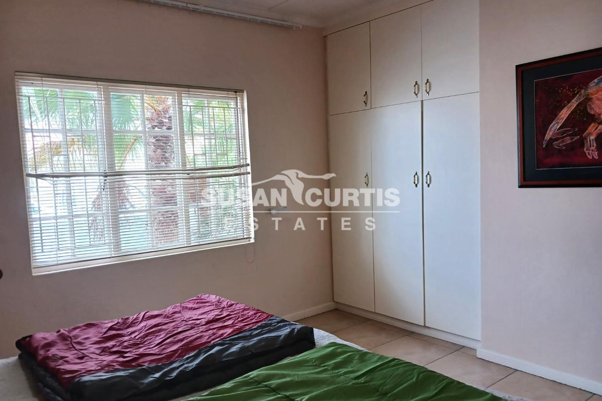 A bedroom featuring built-in cupboards and a window with fitted blinds, providing natural light and storage space.