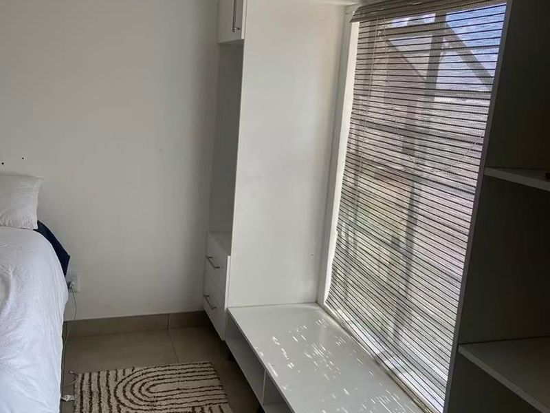 A bedroom featuring built-in white cabinetry with an integrated window seat and roller blind, complemented by neutral tiled flooring.
